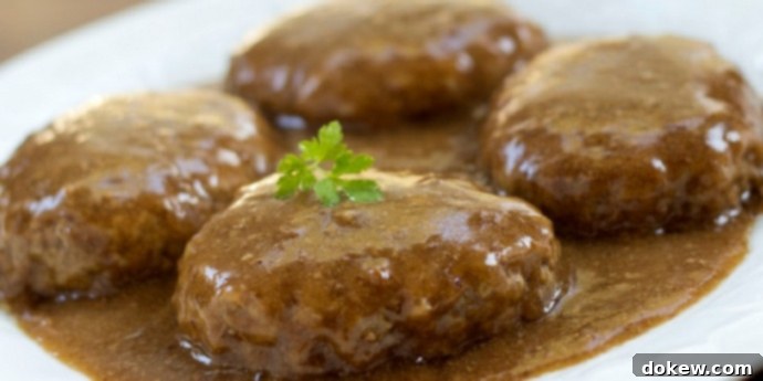 Simple Salisbury Steak Recipe White plate with hamburger patties covered with rich brown gravy, garnished with fresh parsley, ready to serve.