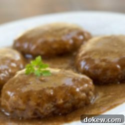 Homestyle Salisbury Steak 2 Simple Salisbury Steak patties covered with savory brown gravy and a sprig of parsley on a white plate.
