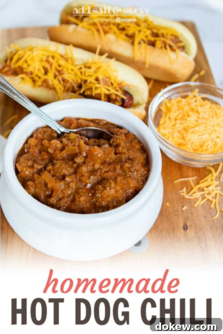 Classic Hot Dog Chili 2 A high-angle shot showcasing a bowl of homemade hot dog chili, two chili cheese dogs loaded with shredded cheddar, and a small dish of extra cheese, all presented on a wooden board. Ideal for Pinterest saving.
