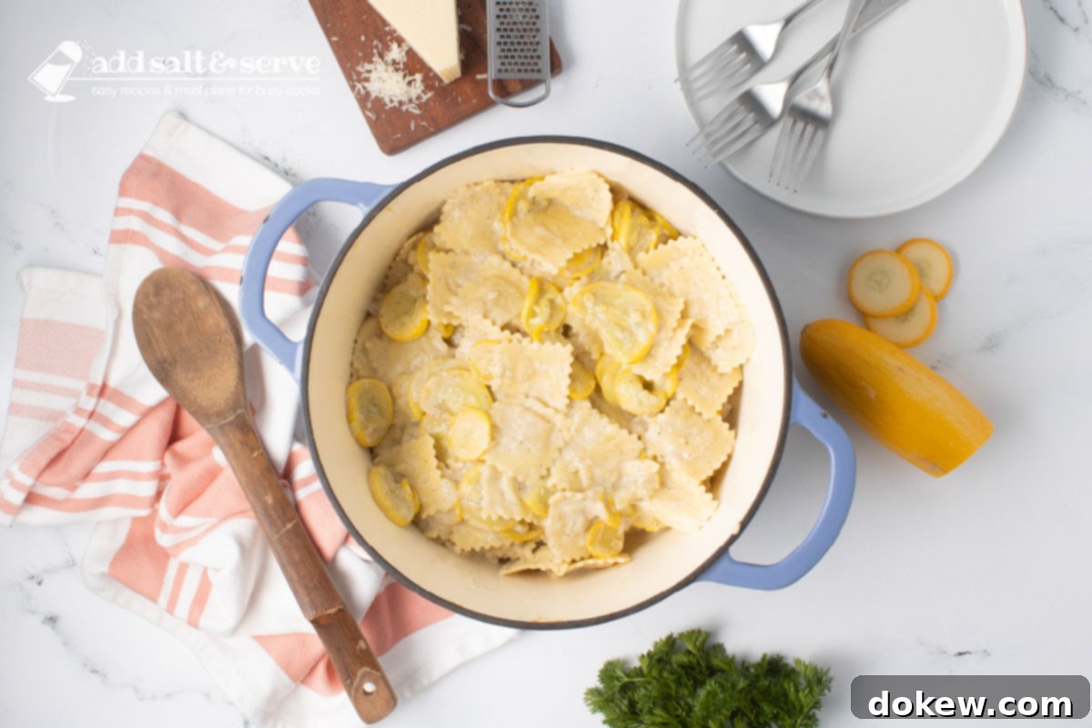 Velvety 20-Minute Summer Squash Ravioli 9 Dutch oven with cooked cheese ravioli mixed with Parmesan cheese and sautéed summer squash and onion beside a wooden spoon and surrounded by fresh squash, a bunch of parsley, and a block of fresh Parmesan cheese.