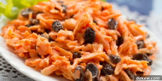 Carrot Raisin salad on a white plate garnished with celery leaves, a refreshing summer side dish