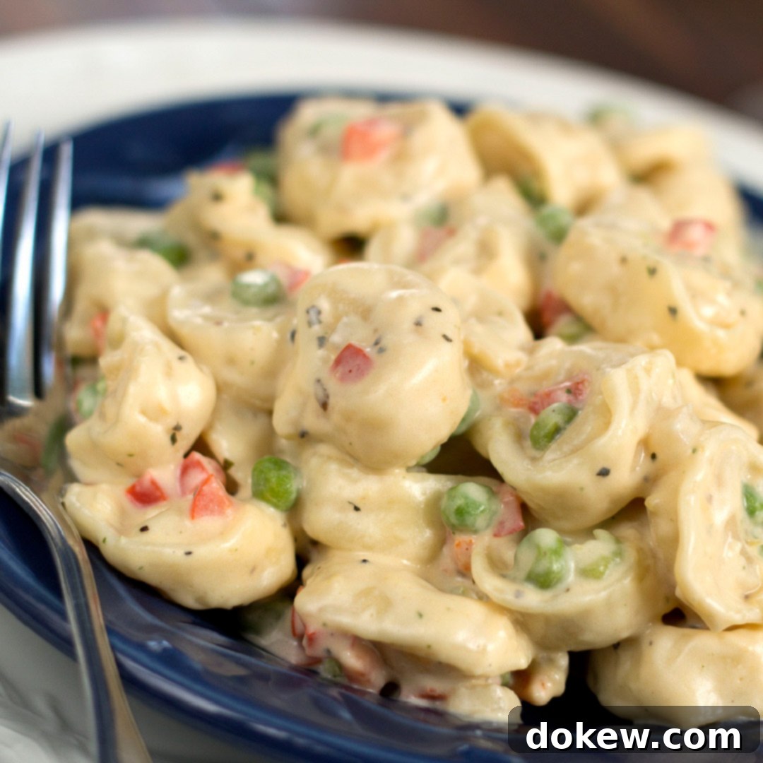 Dreamy Creamy Tortellini 2 A blue plate with a fork and tortellini, peas, and diced bell peppers covered in cream sauce.