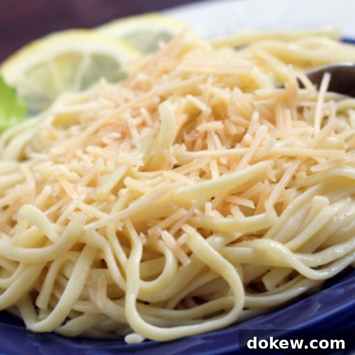 Zesty Lemon Parmesan Pasta 2 Cooked spaghetti on a blue plate with a fork. The plate is garnished with two lemon slices and a sprig of parsley.