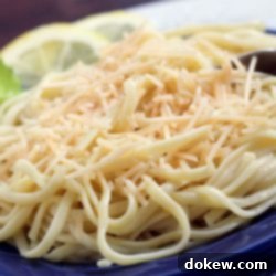 Zesty Lemon Parmesan Pasta 3 Cooked spaghetti on a blue plate with a fork. The plate is garnished with two lemon slices and a sprig of parsley.