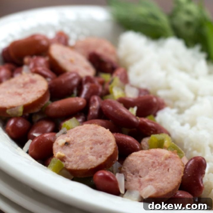 Crafting Distinct English Titles 2 Slices of smoked sausage mixed with red beans, diced onions, and diced green bell pepper, beside a serving of rice. The food is in a white bowl with a fork and garnished with a sprig of parsley.