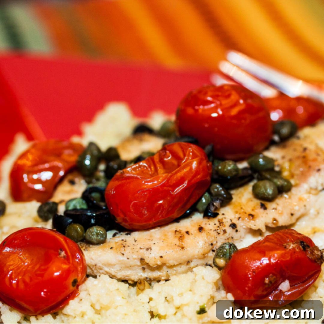 Succulent chicken breast, perfectly cooked, resting on a bed of fluffy couscous. It's generously garnished with vibrant cherry tomatoes, thinly sliced black olives, and briny capers, all served on an elegant red plate with a fork poised for a delicious bite. This Mediterranean-inspired dish is ideal for quick, healthy, and easy weeknight dinners.