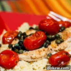Vibrant Mediterranean Chicken with Capers 3 Succulent chicken breast, perfectly cooked, resting on a bed of fluffy couscous. It's generously garnished with vibrant cherry tomatoes, thinly sliced black olives, and briny capers, all served on an elegant red plate with a fork poised for a delicious bite. This Mediterranean-inspired dish is ideal for quick, healthy, and easy weeknight dinners.