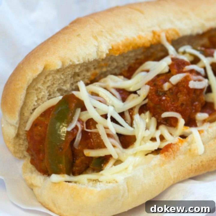 Meatballs, sauce, shredded mozzarella cheese, and strips of bell peppers on a hot dog bun, all on a white plate.