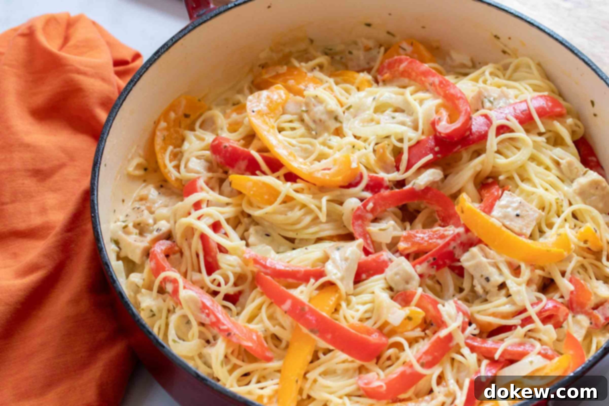 Chicken Pepper Pasta Pasta with chicken, sliced onion, and strips of red and yellow bell peppers cooked in a white sauce in a skillet.