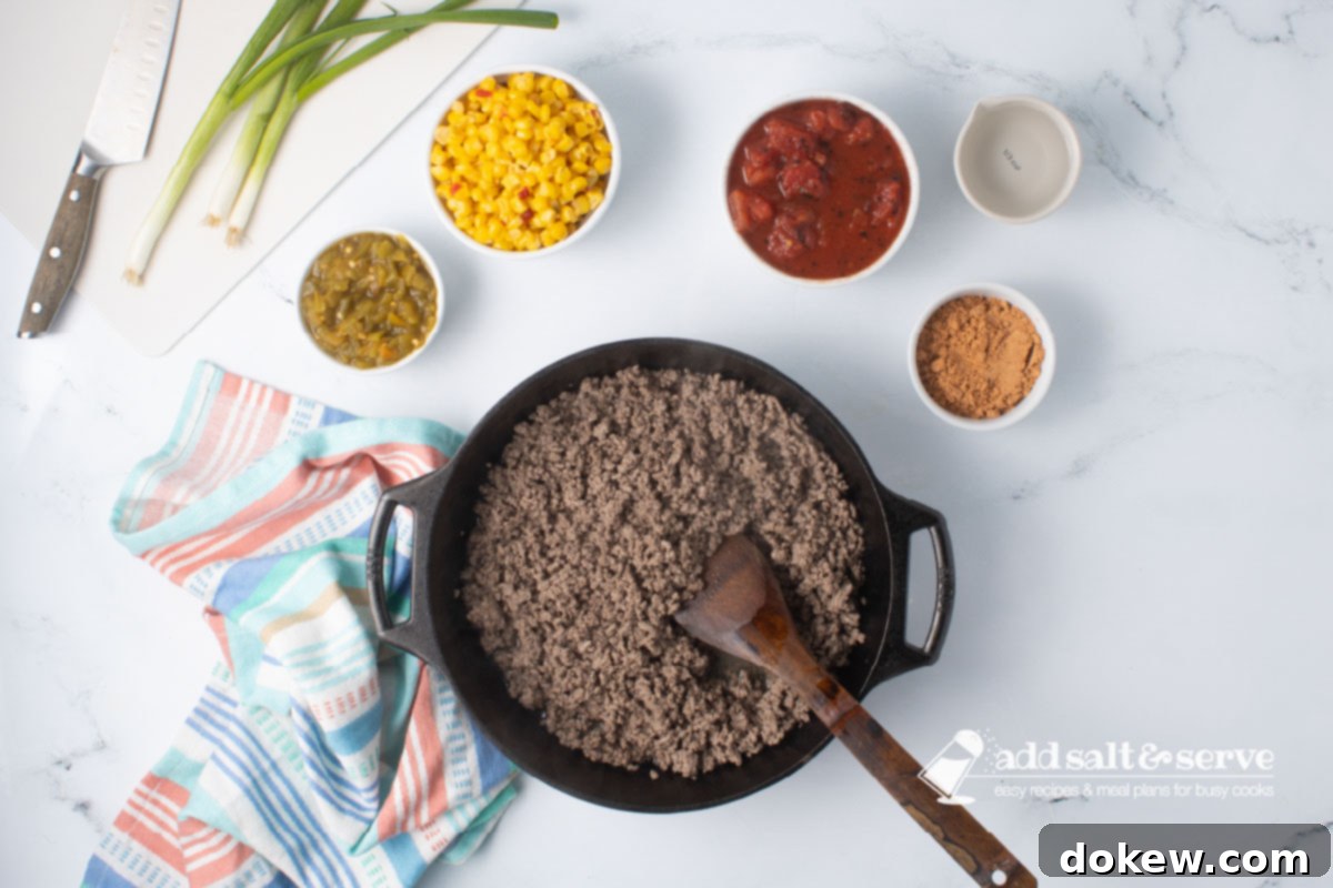 Fiesta Spaghetti 4 A cast iron skillet with cooked ground beef next to bowls of green chiles, Mexi-corn, fire-roasted diced tomatoes, taco seasoning, and water.