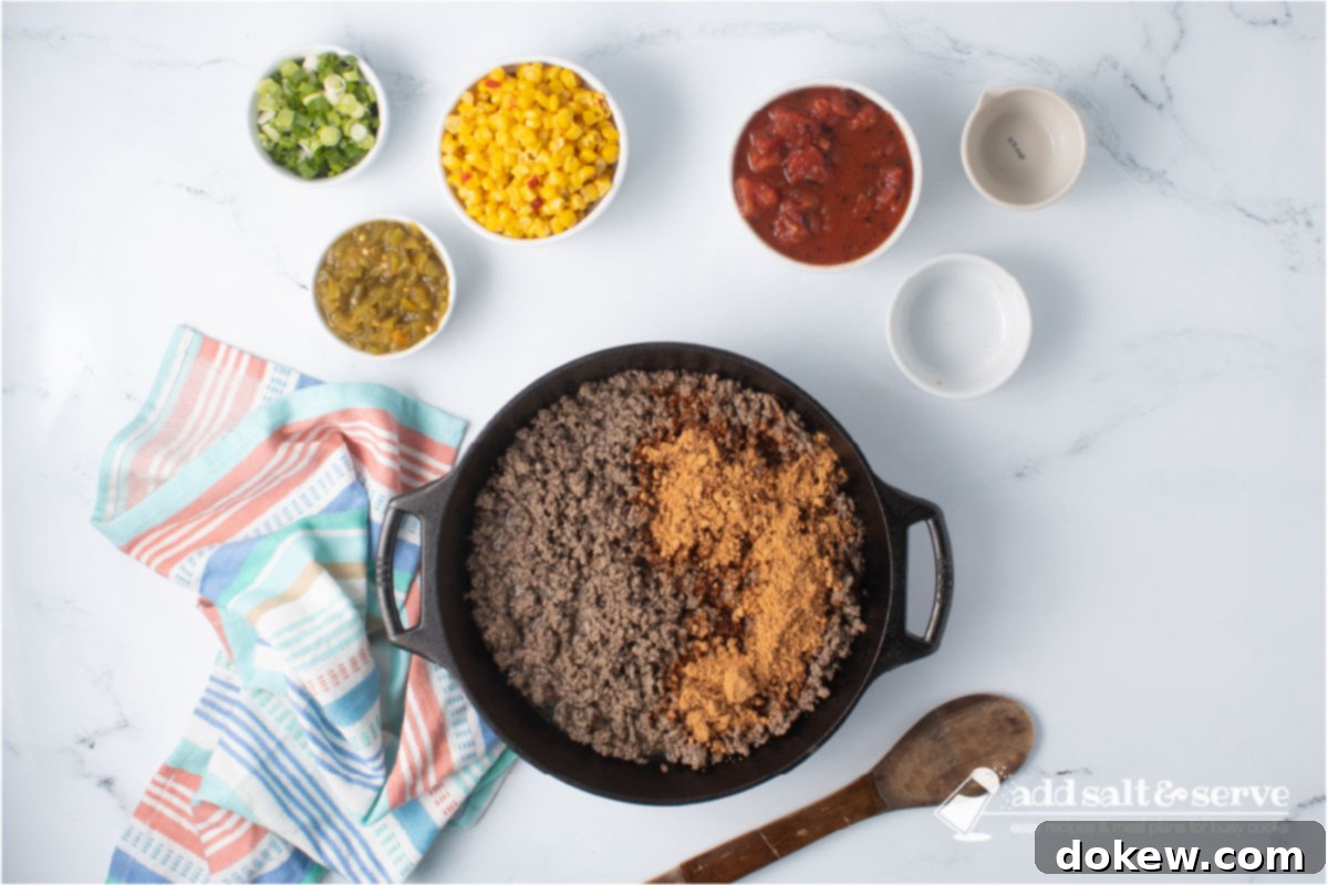 Fiesta Spaghetti 5 Cooked ground beef in a cast iron skillet with taco seasoning and water, surrounded by other ingredients.