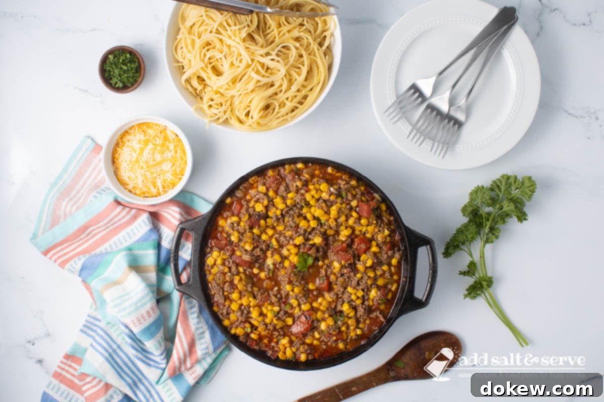 Fiesta Spaghetti 7 A cast iron skillet of Mexican Spaghetti sauce, with cooked spaghetti and shredded cheese on the side.