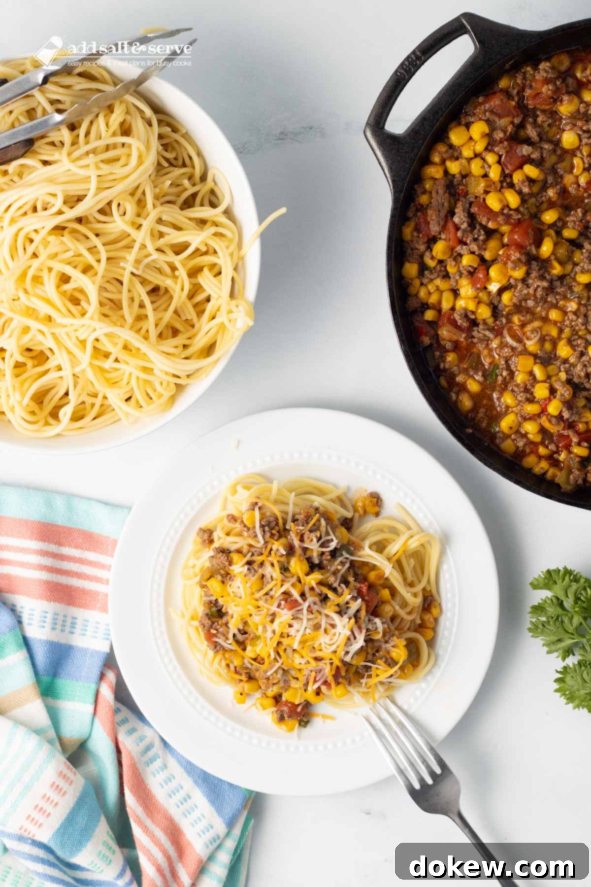 Fiesta Spaghetti 9 A plate of Mexican Spaghetti topped with shredded cheese, next to a pot of the sauce and a bowl of cooked spaghetti.