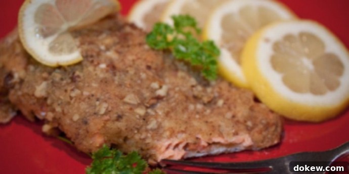 Pecan Crusted Salmon Pecan crusted salmon on a red plate with a fork, garnished with lemon slices and sprigs of parsley.