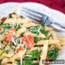 Vibrant Carbonara with Tomato and Spinach 2 White plate with penne pasta, cooked baby spinach, cherry tomatoes, and shredded mozzarella cheese. There is a fork on the plate.
