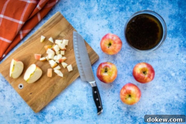 apple-raisin-salad-ip-6-min Overhead view of a chopping board with shopped apple and a knife, four apples to the side, a bowl of raisins soaking in water, all on a blue surface with a coral towel laying to the side.